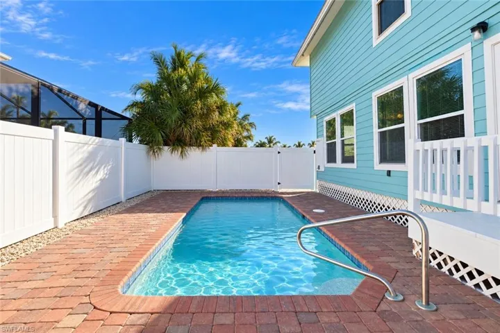 Private backyard featuring an in-ground swimming pool, decorative brick paver decking, and solid white privacy fencing - Virtually Edited Image