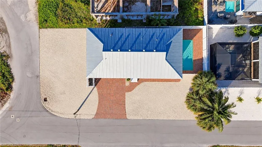 Aerial perspective featuring a metal roof, brick paver driveway, gravel landscaping, and a rectangular swimming pool with an attached screen enclosure - Virtually Edited Image