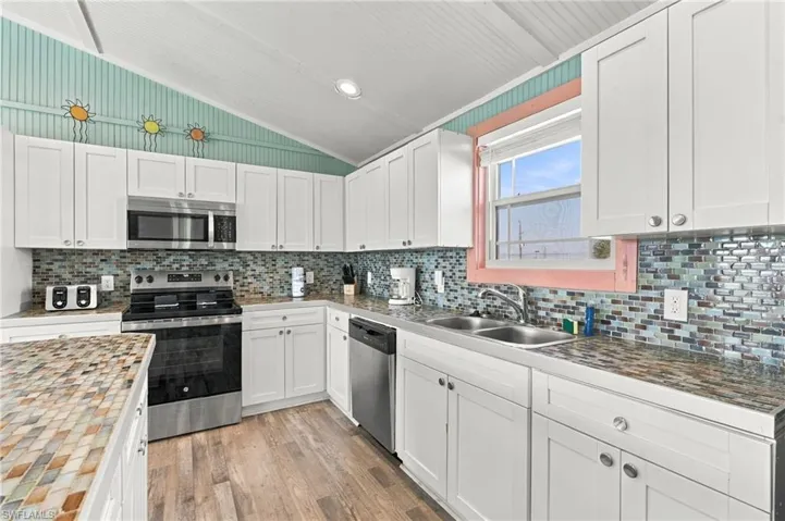 Kitchen featuring white shaker-style cabinetry, mosaic tile backsplash, wood-finish flooring, and stainless steel appliances - Virtually Edited Image