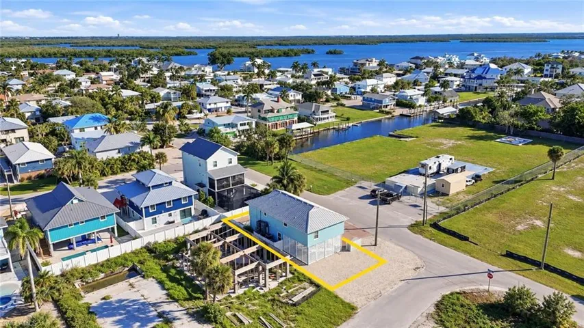 Aerial perspective of a multi-story coastal property featuring a metal roof, elevated foundation, and proximity to a canal - Virtually Edited Image