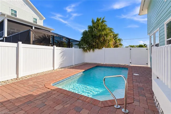Private backyard featuring a rectangular swimming pool, red brick paver decking, and a full-height white vinyl privacy fence - Virtually Edited Image