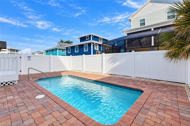 In-ground swimming pool with a handrail, enclosed by a white vinyl privacy fence and surrounded by paver patio hardscaping - Virtually Edited Image