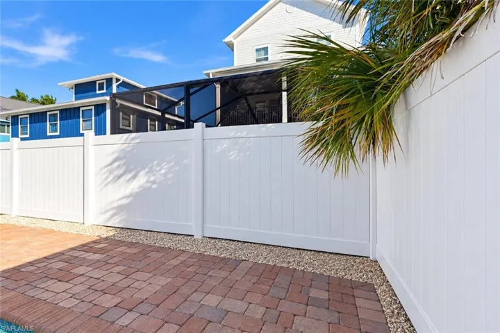 White vinyl privacy fencing enclosing a patio finished with red-tone concrete pavers and gravel border - Virtually Edited Image