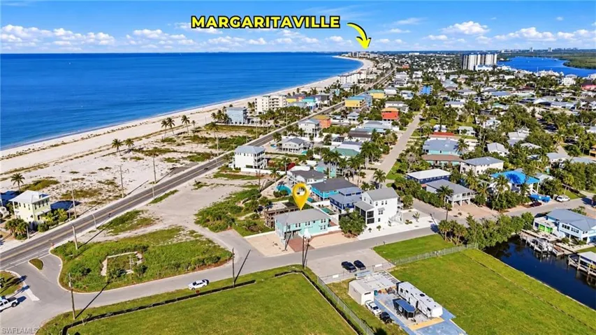 Aerial perspective of coastal residential property featuring proximity to the shoreline, paved street access, and surrounding natural vegetation - Virtually Edited Image