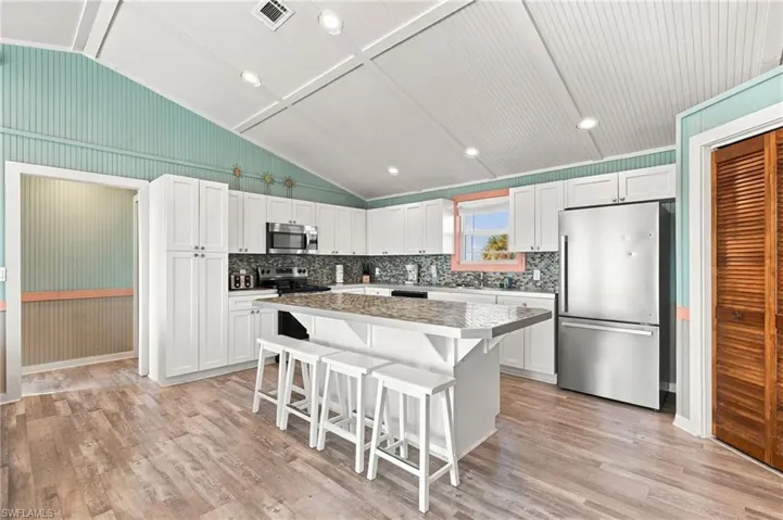 Kitchen featuring white cabinetry, center island with stone-finish countertop, stainless steel appliances, recessed ceiling lighting, and wood-finish flooring - Virtually Edited Image