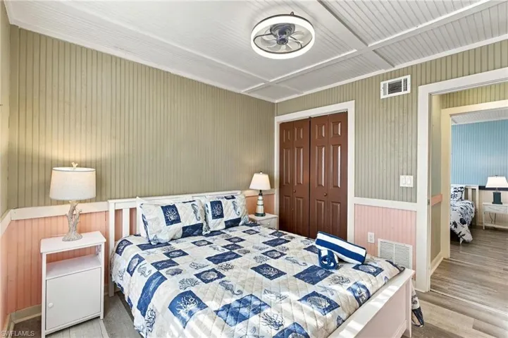 Beadboard wall paneling, coffered ceiling, flush-mount circular LED light fixture, wood-finish flooring, and double-door closet - Virtually Edited Image