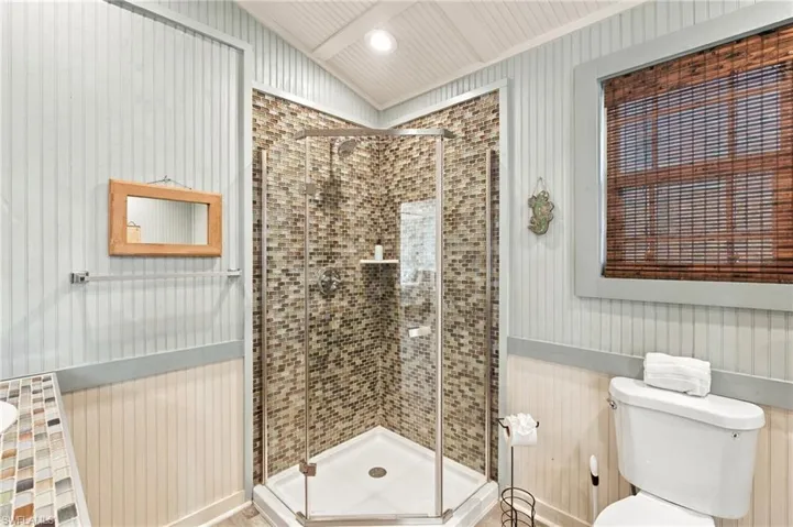 Shower stall with a glass enclosure and mosaic tile surround, beadboard wall paneling, and a built-in corner shelf - Virtually Edited Image