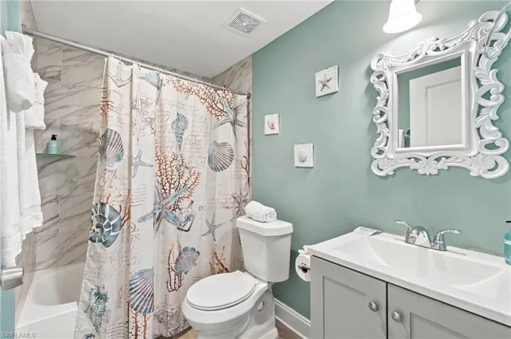 Bathroom featuring a vanity with a white integrated basin, dual-handle polished chrome faucet, wall-mounted light fixture, and a shower-tub combination with stone-patterned wall tile - Virtually Edited Image