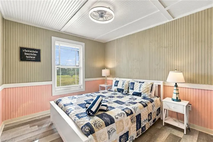 Beadboard wall paneling with chair rail molding, wood-finish flooring, ceiling with exposed beams, and flush-mount LED ceiling fixture - Virtually Edited Image