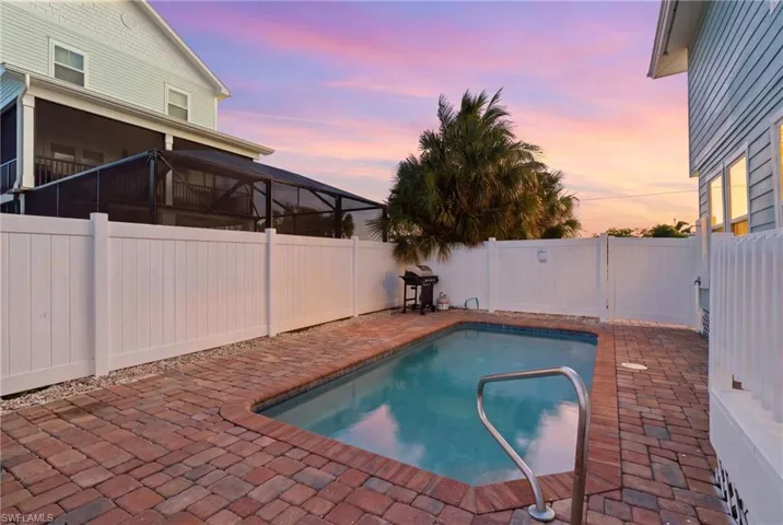 Private backyard featuring a swimming pool, red brick paver decking, white vinyl privacy fencing, and a screened-in porch - Virtually Edited Image