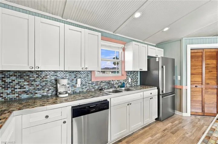 Kitchen featuring white shaker-style cabinetry, mosaic tile backsplash, wood-finish flooring, beadboard ceiling, and stainless steel appliances - Virtually Edited Image