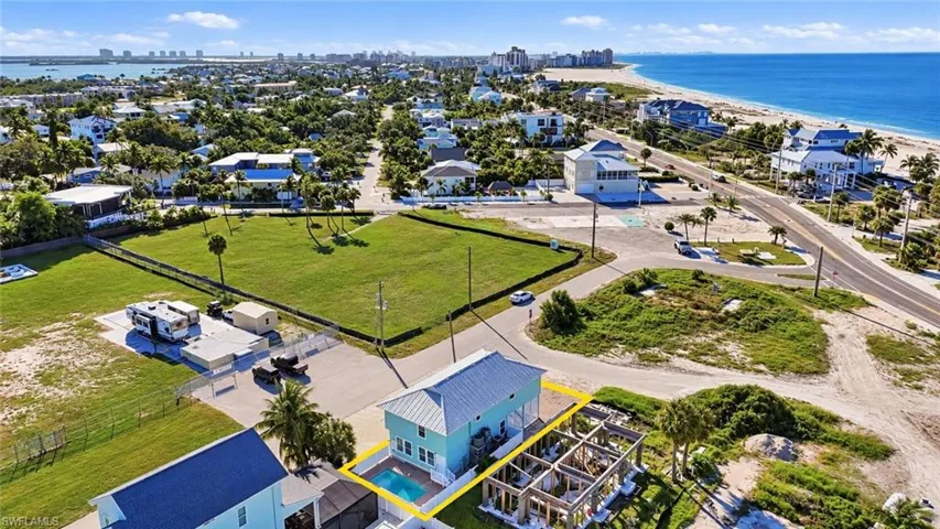 Aerial perspective of coastal property featuring a multi-story residence with a metal roof, an in-ground swimming pool, and proximity to the shoreline - Virtually Edited Image