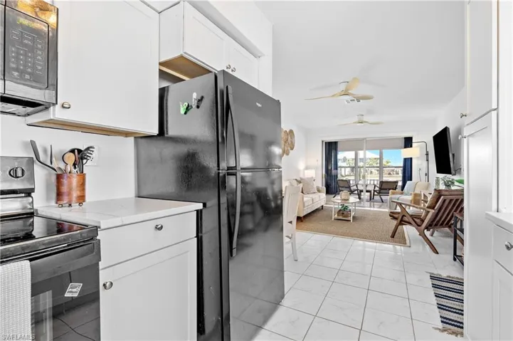 Kitchen with black appliances, white cabinetry, a ceiling fan, open floor plan, and light marble finish floors
