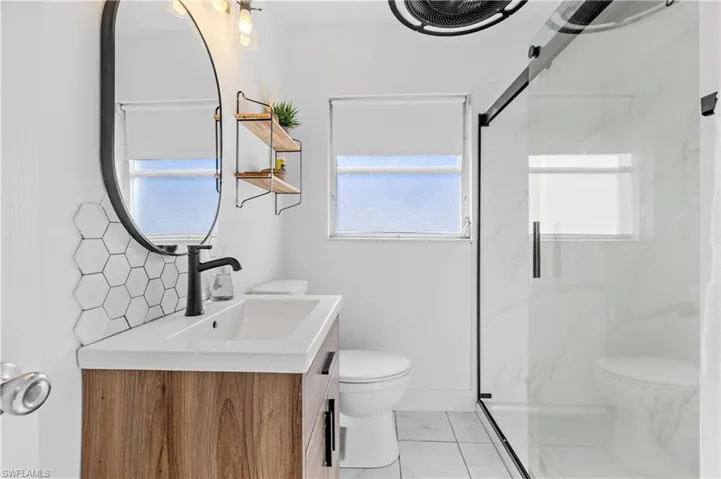 Bathroom with vanity, plenty of natural light, a marble finish shower, and light marble finish flooring