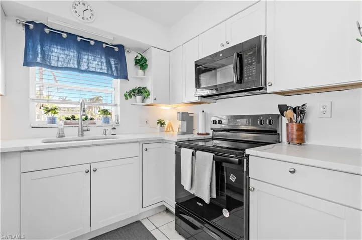 Kitchen with black appliances, white cabinetry, light stone counters, and open shelves