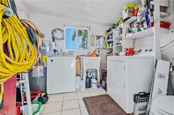 Washroom with washing machine and clothes dryer, light tile patterned floors, and electric water heater
