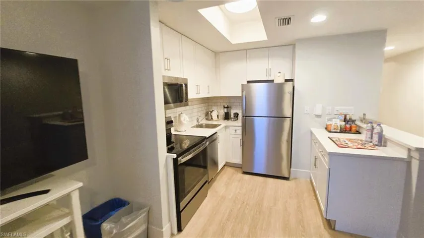Kitchen with appliances with stainless steel finishes, light wood-style flooring, white cabinetry, backsplash, and a skylight