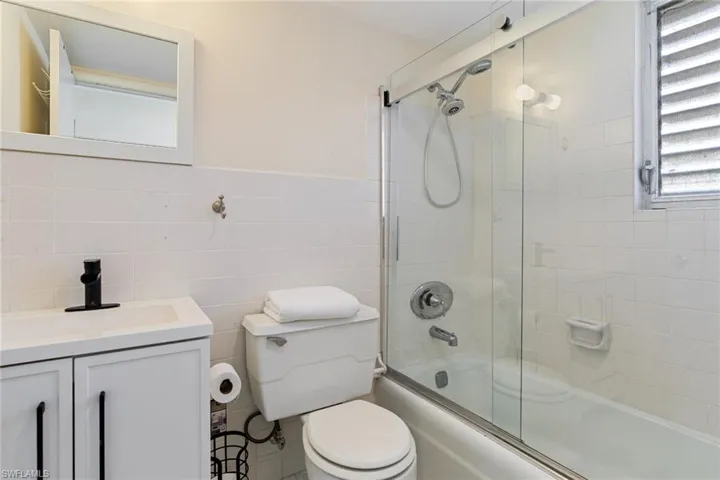 Full bathroom with vanity, tile walls, combined bath / shower with glass door, and wainscoting