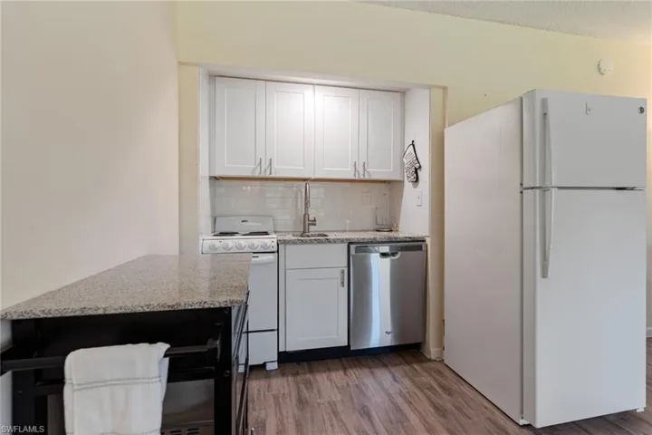 Kitchen with white appliances, white cabinets, and light stone counters