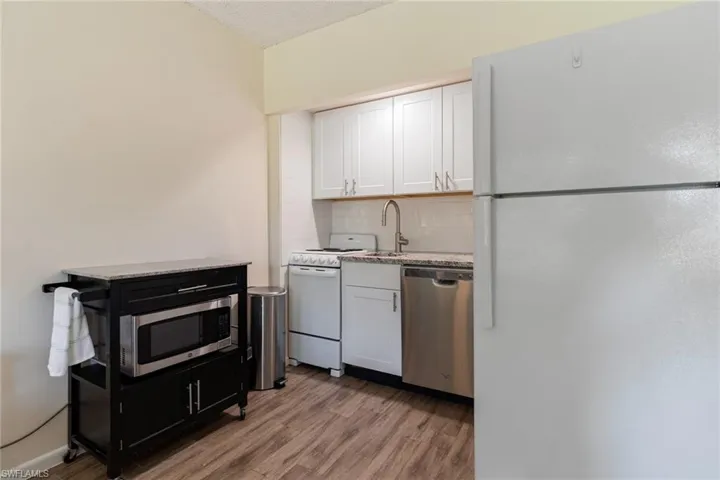 Kitchen with stainless steel appliances, white cabinetry, light wood-style flooring, light stone countertops, and tasteful backsplash