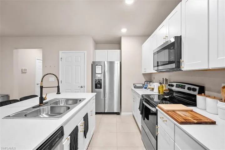 Kitchen featuring light tile patterned floors, appliances with stainless steel finishes, sink, and white cabinets