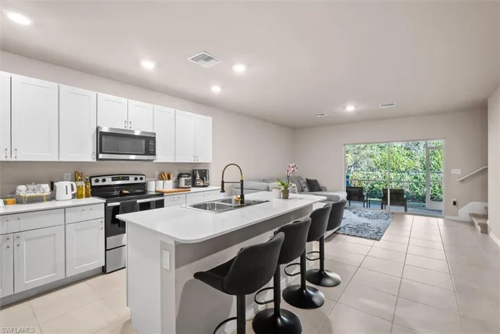Kitchen with sink, appliances with stainless steel finishes, white cabinetry, a kitchen breakfast bar, and a center island with sink