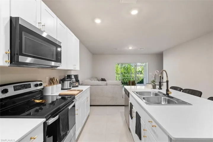 Kitchen featuring sink, white cabinetry, a center island with sink, light tile patterned floors, and appliances with stainless steel finishes