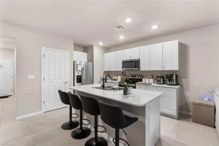 Kitchen with appliances with stainless steel finishes, white cabinetry, sink, a kitchen breakfast bar, and a kitchen island with sink