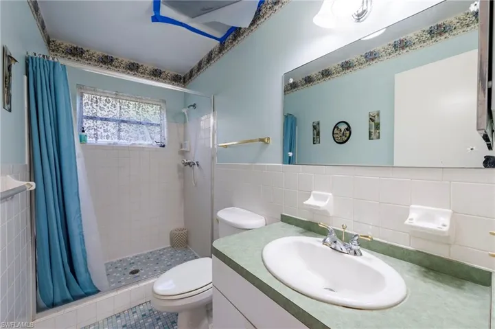 Bathroom featuring walk in shower, tile walls, vanity, and toilet