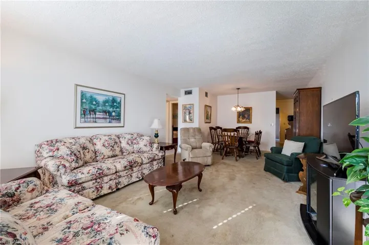 Carpeted living room featuring a textured ceiling, a notable chandelier, and a wood stove