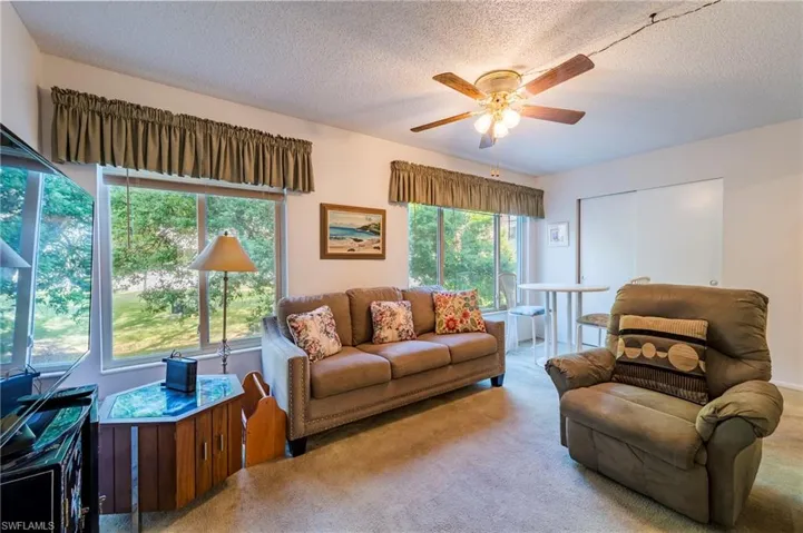 Carpeted living room featuring a textured ceiling, ceiling fan, and plenty of natural light