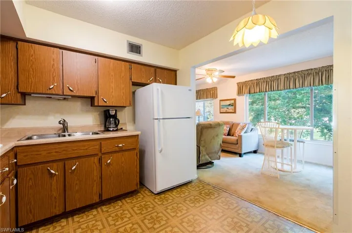 Kitchen featuring white fridge, a textured ceiling, ceiling fan, sink, and light colored carpet