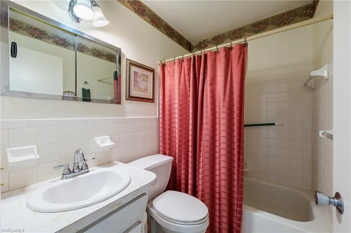 Full bathroom with tile walls, shower / tub combo, vanity, and toilet