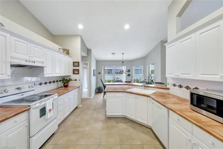 Kitchen featuring white cabinets, white appliances, hanging light fixtures, and wood counters