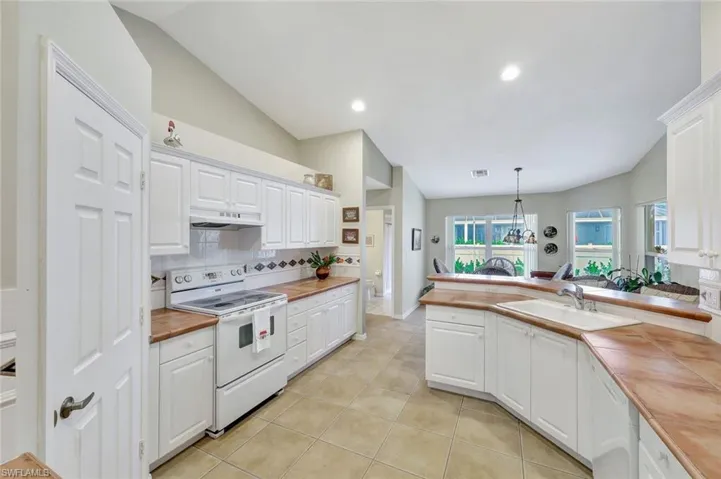 Kitchen with pendant lighting, white cabinets, butcher block counters, and electric range