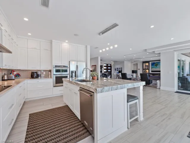 Kitchen featuring white cabinetry, sink, backsplash, a center island with sink, and appliances with stainless steel finishes