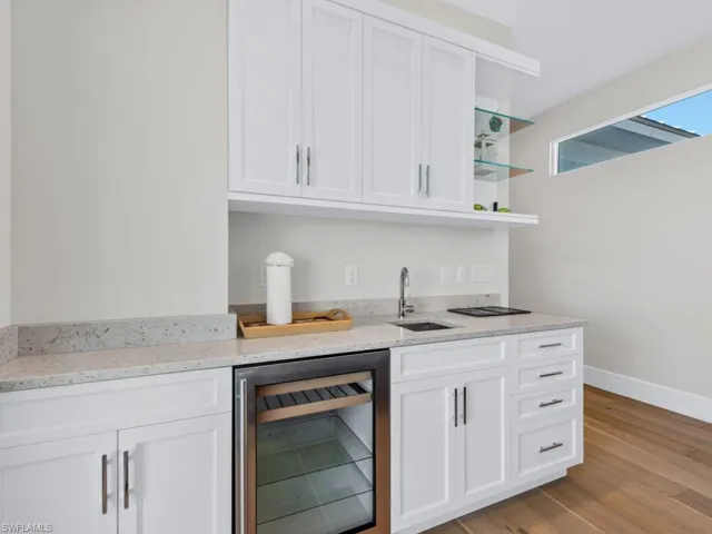 Kitchen featuring light stone countertops, beverage cooler, sink, light hardwood / wood-style flooring, and white cabinets