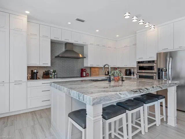 Kitchen featuring a kitchen breakfast bar, wall chimney range hood, stainless steel appliances, and an island with sink
