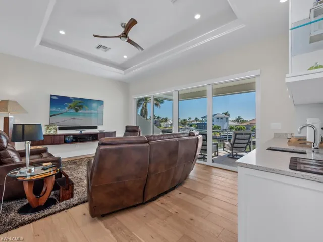 Living room featuring light wood-type flooring, a raised ceiling, ceiling fan, and sink