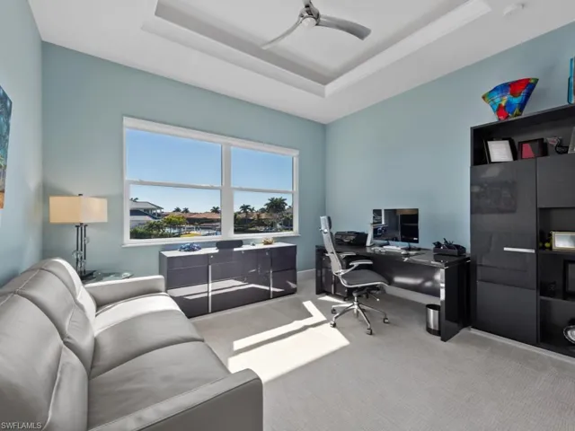 Carpeted office featuring a raised ceiling and ceiling fan