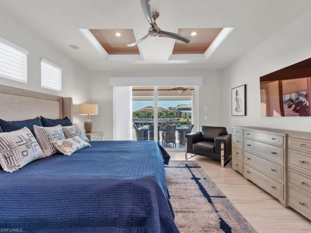 Bedroom with access to exterior, a raised ceiling, multiple windows, and ceiling fan