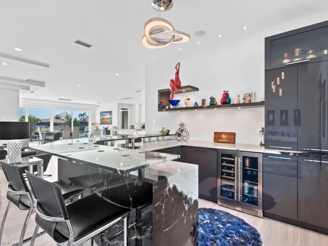Bar featuring decorative light fixtures, light stone counters, light wood-type flooring, and beverage cooler