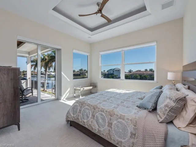 Carpeted bedroom featuring access to exterior, a raised ceiling, multiple windows, and ceiling fan