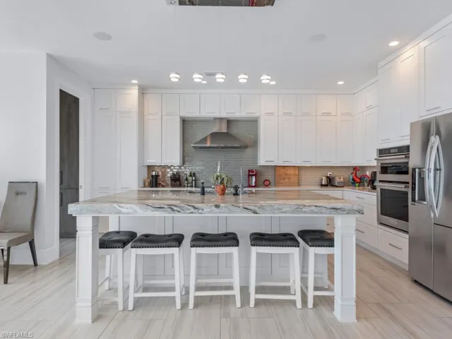 Kitchen featuring a center island with sink, wall chimney exhaust hood, white cabinetry, and appliances with stainless steel finishes