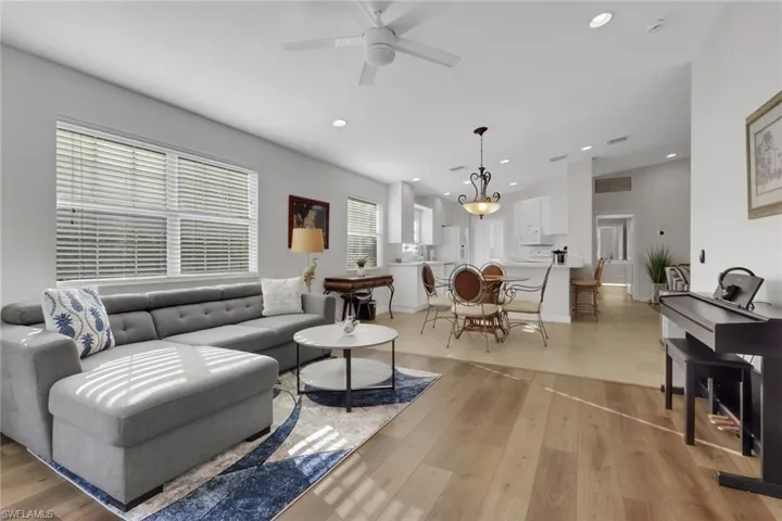Open-concept main room featuring wood-finish flooring, recessed lighting, white cabinetry, a center island with counter seating, and a decorative pendant light fixture