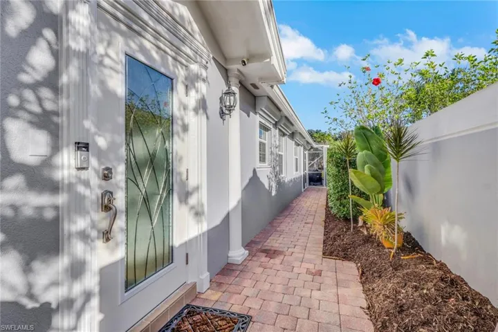 Exterior entry featuring a glass-inset door, decorative column, brick paver walkway, and manicured garden bed