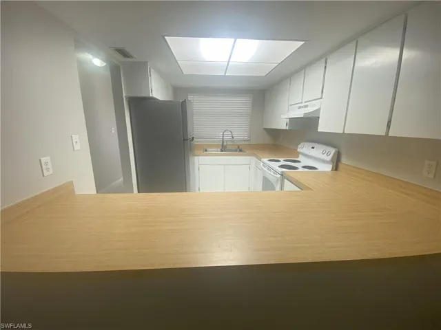 Kitchen with white cabinetry, white electric stove, freestanding refrigerator, light countertops, and under cabinet range hood