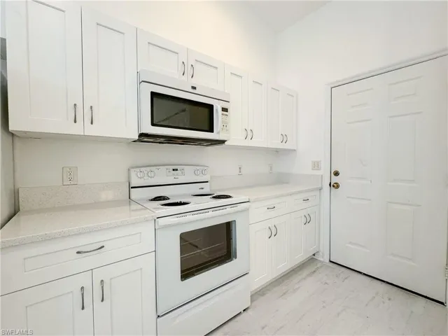 Kitchen featuring light stone countertops, white appliances, and white cabinets