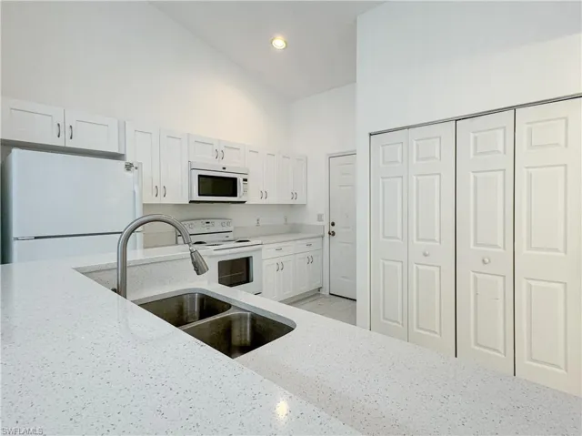 Kitchen with white cabinetry, sink, light stone counters, high vaulted ceiling, and white appliances