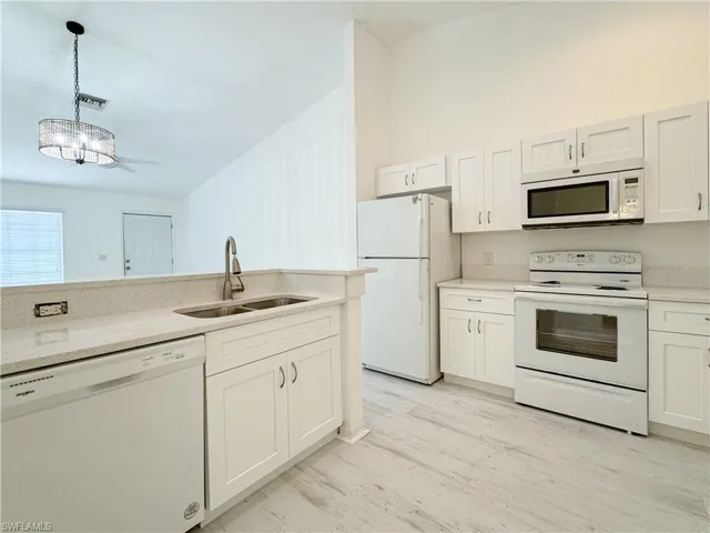 Kitchen with light wood-type flooring, pendant lighting, white cabinetry, sink, and white appliances